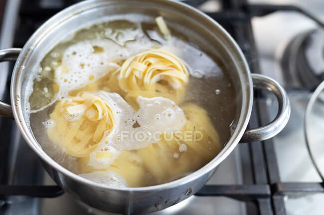 Close up top view of some linguine pasta boiling in a pot in the kitchen. Social distancing and self isolation in quarantine lockdown. — Stock Photo