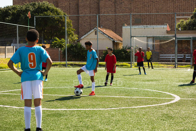 Rear view of two teams of multi-ethnic boy soccer players wearing their team strips, in action during a soccer match on a playing field — Stock Photo