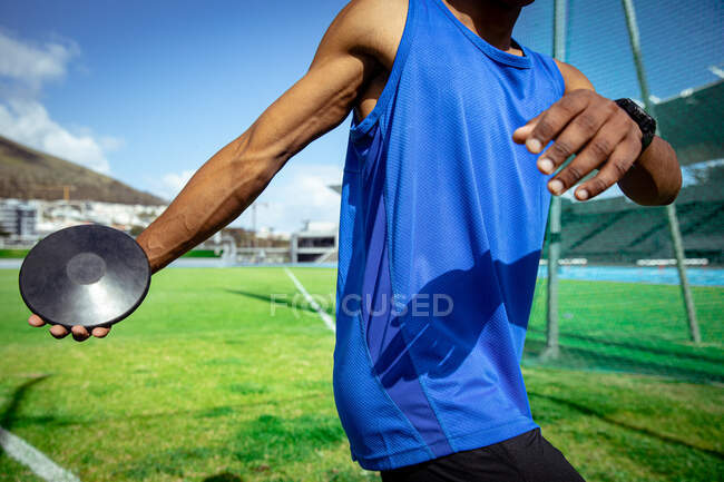 Side view mid section of a mixed race male athlete practicing at a sports stadium, preparing to throw a discus — Stock Photo