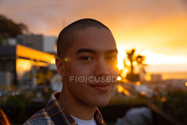 Портрет змішаної раси людини, що висить на терасі на даху з небом заходу сонця, дивлячись на камеру і посміхаючись — стокове фото