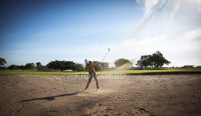 Vista laterale di un uomo caucasico in un campo da golf in una giornata di sole con cielo blu, colpendo una pallina da golf — Foto stock