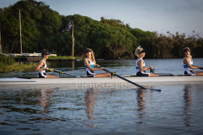 Бічний погляд на веслувальну команду з чотирьох кавказьких жінок, які тренуються на річці, веслуючи в черепашці. — стокове фото