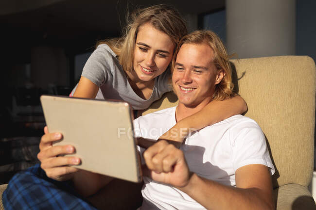 Casal caucasiano sentado em uma varanda, abraçando e usando um tablet digital. Distanciamento social e auto-isolamento em quarentena. — Fotografia de Stock