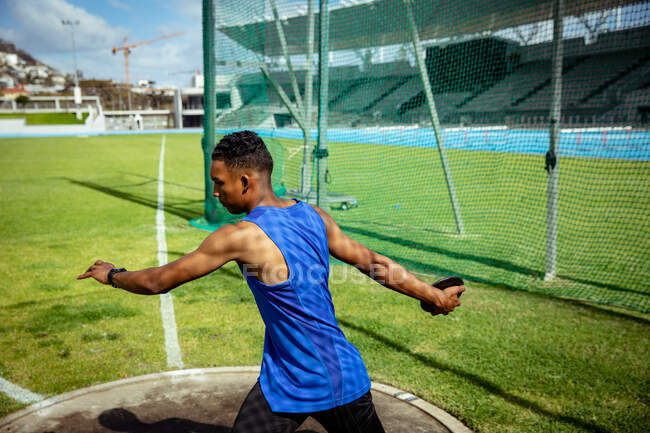 Side view of a mixed race male athlete practicing at a sports stadium, preparing to throw a discus. Track and Field Sports Training in Stadium. — Stock Photo