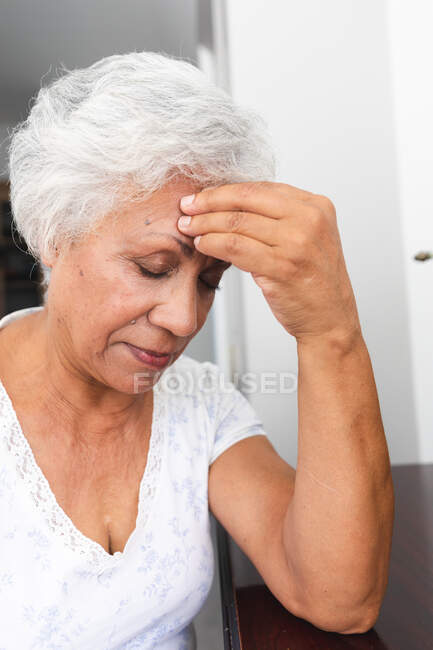 Primo piano di una attraente donna afroamericana anziana in pensione a casa nella sua camera da letto con mal di testa, toccandosi la testa con gli occhi chiusi, auto-isolante durante la pandemia di coronavirus19 — Foto stock