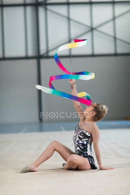 Vista laterale della ginnasta caucasica adolescente che si esibisce in palestra, si allena con il nastro, indossa un body multicolore. — Foto stock
