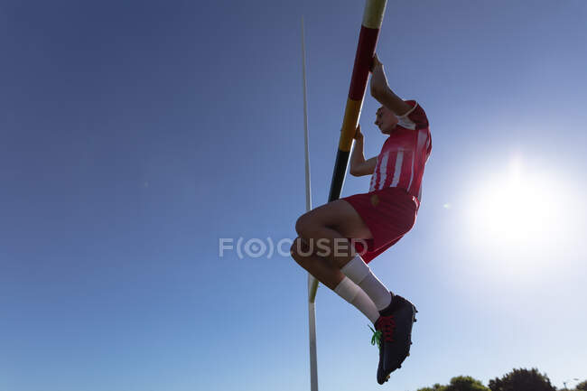 Low angle side view of a teenage Caucasian male rugby player wearing red and white team strip, doing pull ups hanging from the goal on the playing field — Stock Photo