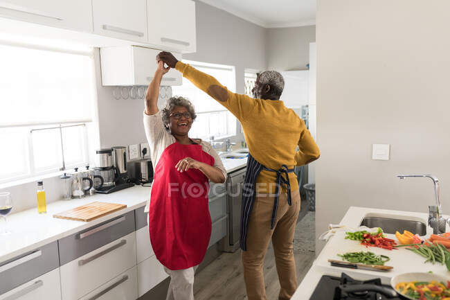 Un couple afro-américain âgé passe du temps à la maison ensemble, la distance sociale et l'isolement personnel en quarantaine pendant l'épidémie de coronavirus covid 19, dansant dans la cuisine — Photo de stock