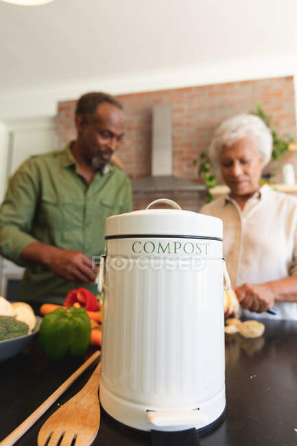 Happy senior retired African American couple at home, preparing vegetables to make a meal, a container for composting the green waste in the foreground, couple at home together isolating during coronavirus covid19 pandemic — Stock Photo