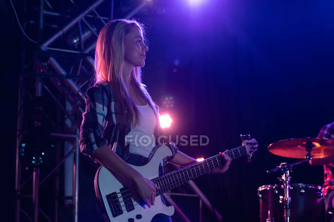 Side view of a Caucasian woman with long blonde hair playing a white bass  guitar on