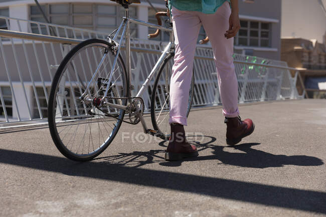 Rear view low section of man with long dreadlocks out and about in the city on a sunny day, walking the street and wheeling his bicycle. — Stock Photo