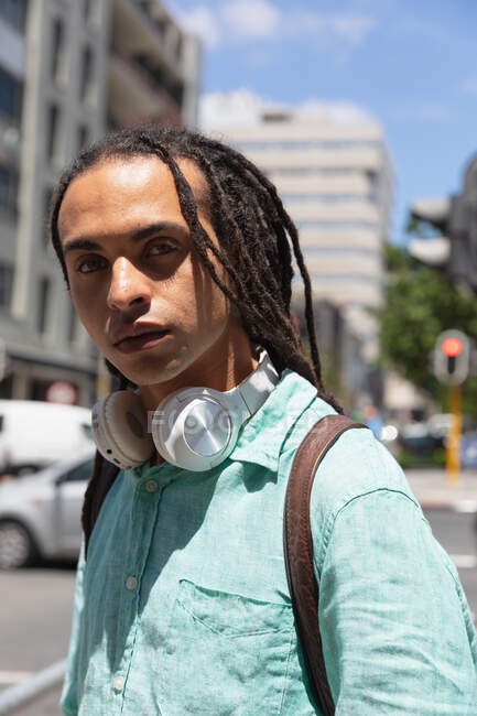 Portrait of a mixed race man with long dreadlocks out and about in the city on a sunny day, standing in the street and looking straight into a camera — Stock Photo