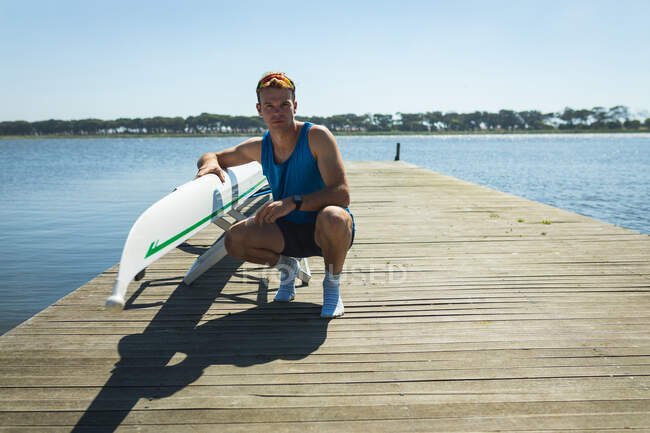 Front view of a Caucasian male rower posing beside a rowing boat on a jetty on the river, looking to camera — Stock Photo