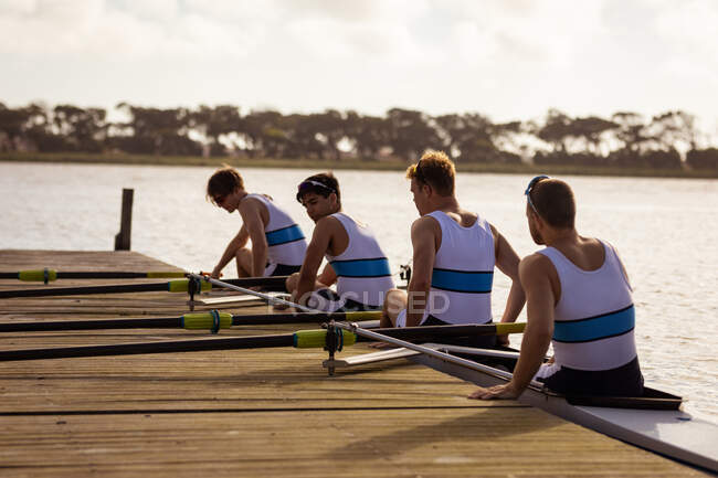 Rear view of a rowing team of four Caucasian men getting out of the rowing boat onto a jetty on the river on a sunny day — Stock Photo