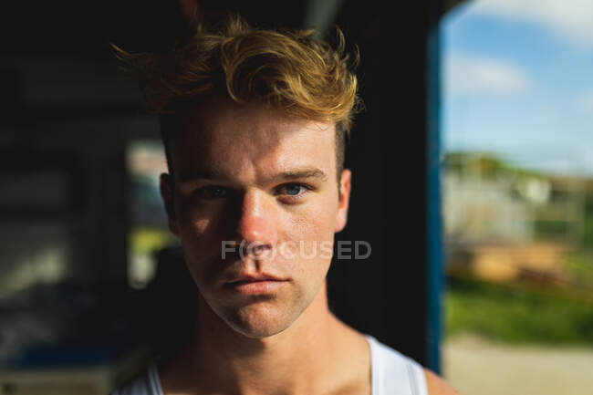 Portrait of a confident Caucasian male rower standing in a boathouse, looking to camera, on a sunny day, with blue sky in the background — Stock Photo