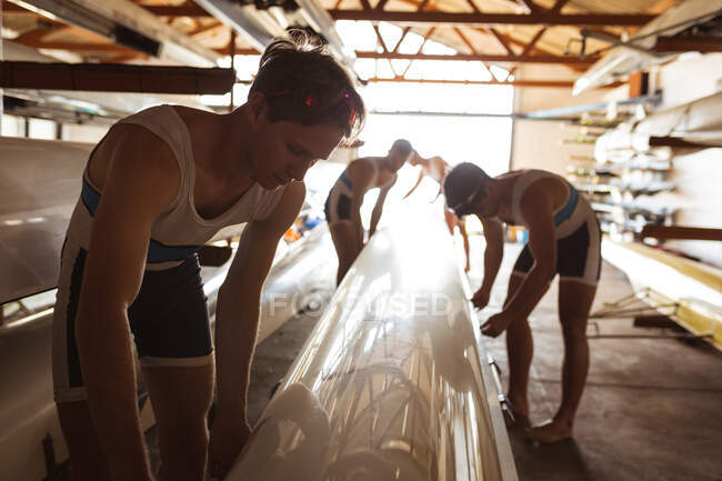 Front view of a rowing team of four Caucasian men putting down a rowing boat in a boathouse on a sunny day — Stock Photo