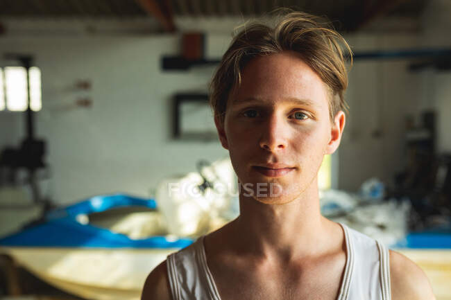 Portrait of a happy Caucasian male rower standing in a boathouse, smiling and looking to camera, with a boat in the background — Stock Photo
