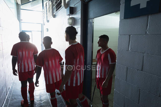 Rear view of a teenage multi-ethnic group of male field hockey players, preparing before a game, walking from the changing room to the pitch, backlit — Stock Photo