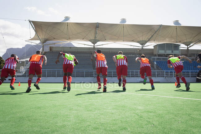 Rear view of a multi-ethnic group of teenage male field hockey players, training before a game, working out on a field hockey pitch, sprinting on a sunny day — Stock Photo