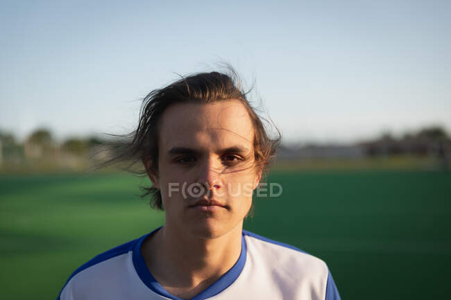 Portrait close up of a Caucasian male field hockey player, wearing a white team strip, standing on a hockey pitch looking to camera on a sunny day — Stock Photo