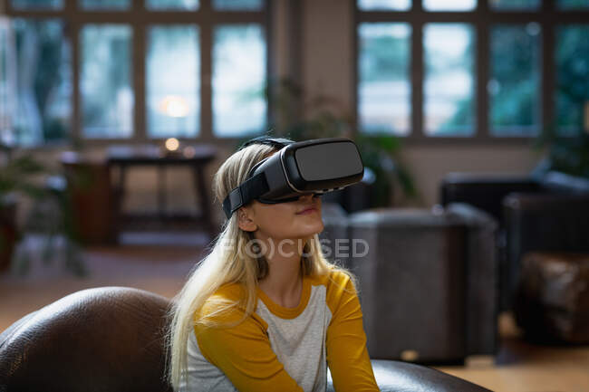 Auto-isolamento em quarentena. vista lateral de uma jovem caucasiana aproveitando o tempo em casa, sentado na sala de estar e usando fones de ouvido vr. — Fotografia de Stock