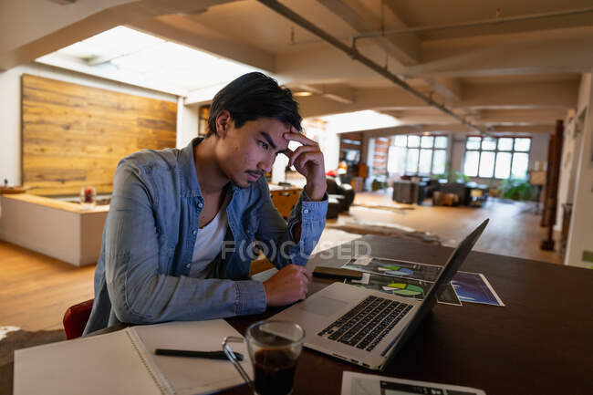 Seitenansicht eines jungen Mannes mit gemischter Rasse, der im Wohnzimmer sitzt und während der Arbeit seinen Laptop benutzt. — Stockfoto