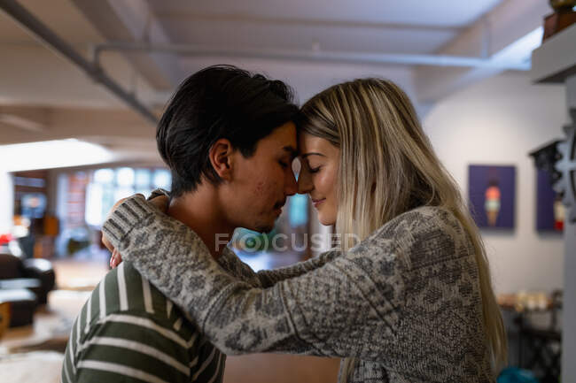 Side view close up of a young Caucasian woman and a young mixed race man, enjoying time at home, standing in their living room, smiling and embracing. — Stock Photo