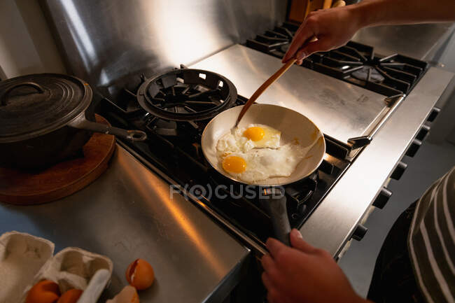 Overhead mid section view of man standing in the kitchen preparing breakfast, frying eggs on a pan. — Stock Photo