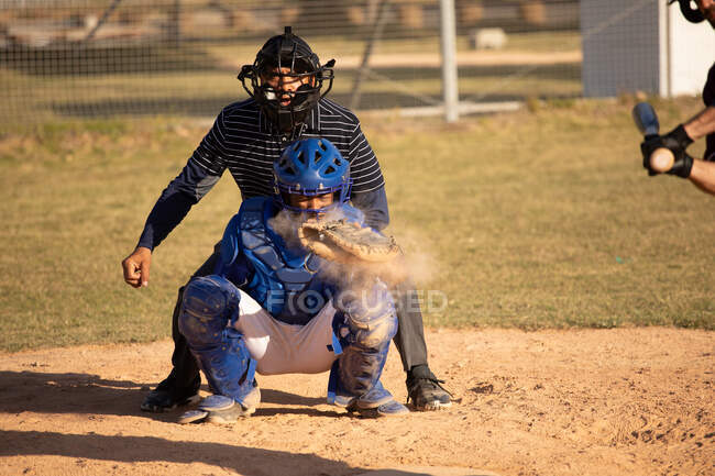 Vista frontal de un jugador de béisbol masculino caucásico durante un partido de béisbol en un día soleado, con un bateador fallando en golpear la pelota y el receptor atrapándolo - foto de stock