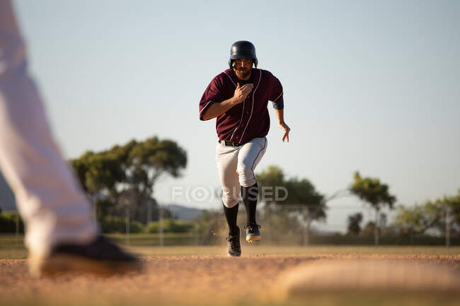 Передній вид на кавказького гравця в бейсбол, під час гри в бейсбол в сонячний день, біжить до бази — стокове фото