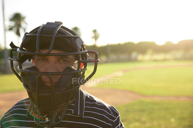 Портрет мужчины-бейсбольного судьи смешанной расы в форме и шлеме, стоящего на бейсбольном поле, смотрящего в камеру — стоковое фото