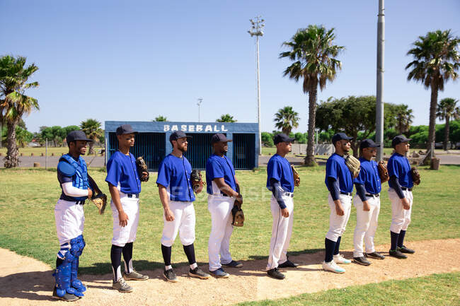 Vue de côté d'un groupe multi-ethnique de joueurs de baseball masculins, se préparant avant un match, debout dans une rangée, se préparant à chanter un hymne national — Photo de stock