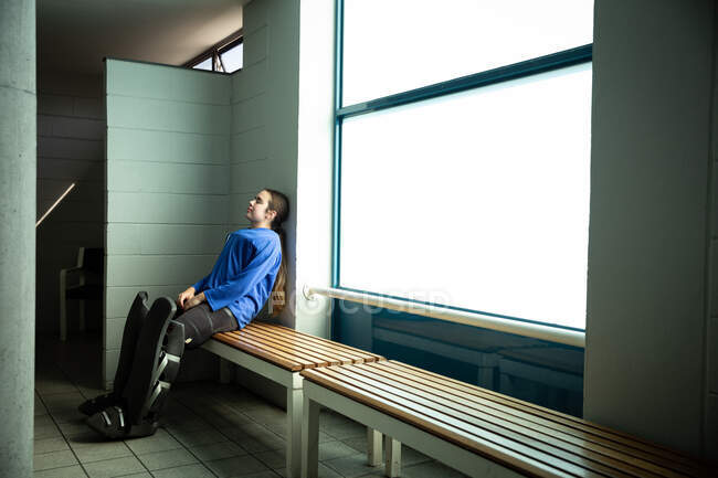 Vue latérale d'une joueuse de hockey sur gazon caucasienne se préparant avant un match, assise dans un vestiaire, appuyée contre un mur — Photo de stock