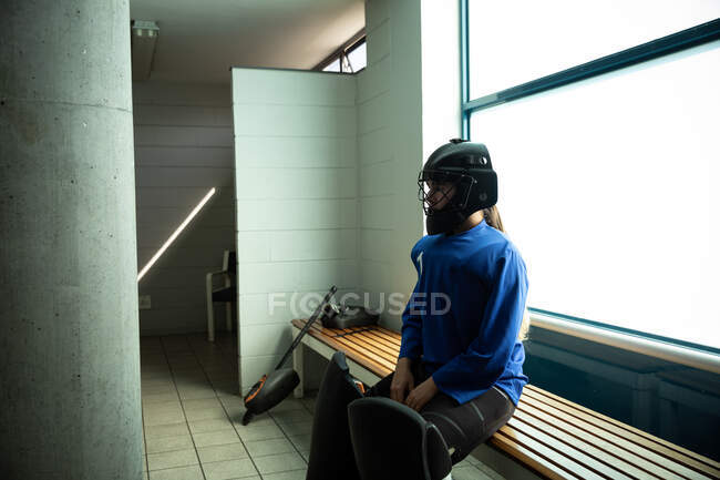 Seitenansicht einer kaukasischen Hockeyspielerin, die sich vor einem Spiel vorbereitet, sitzt in einer Umkleidekabine und trägt einen Eishockeyhelm — Stockfoto