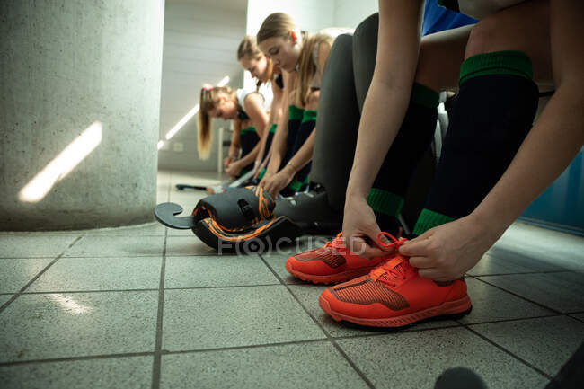 Vue de côté section basse gros plan d'un groupe de joueuses de hockey sur gazon caucasiennes se préparant avant un match, assises dans un vestiaire, attachant leurs chaussures — Photo de stock