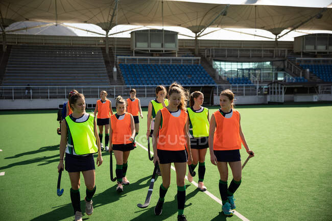 Front view of a group of female Caucasian field hockey players preparing before a game, walking on a hokey pitch, holding hockey sticks — Stock Photo