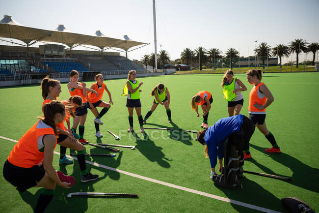 Side view of a group of female Caucasian field hockey players, training before a game, working out on a field hockey pitch, exercising, stretching, on a sunny day — Stock Photo
