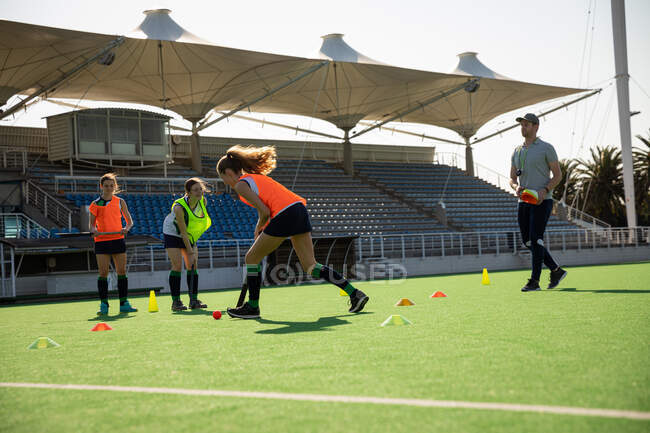Side view mid section of a Caucasian female field hockey player, training before a game, working out on a hockey pitch, exercising, with two her teammates and a coach, on a sunny day — Stock Photo