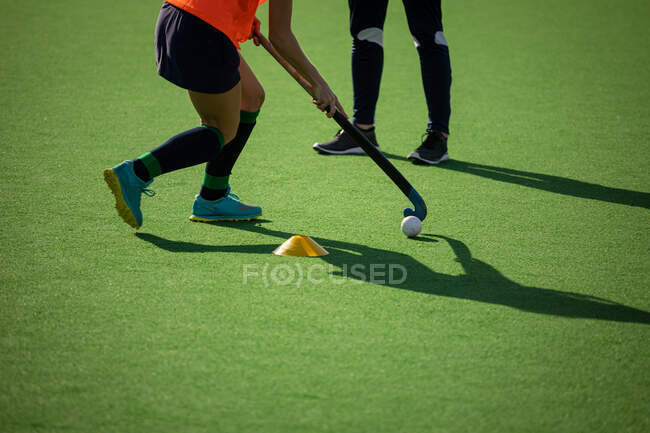 Side view mid section of female field hockey players, training before a game, working out on a hockey pitch, exercising, on a sunny day — Stock Photo