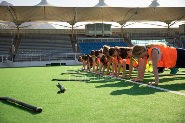 Side view of a group of female Caucasian field hockey players, training before a game, working out on a field hockey pitch, doing push ups, on a sunny day — Stock Photo