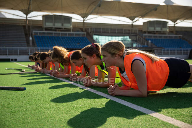 Side view of a group of female Caucasian field hockey players, training before a game, working out on a field hockey pitch, doing planks, on a sunny day — Stock Photo