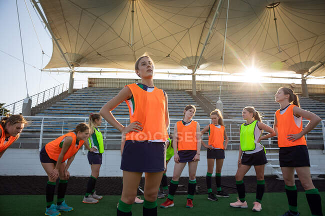 Front view of a group of female Caucasian field hockey players and their Caucasian male coach training before a game, standing on a hockey pitch, resting, on a sunny day — Stock Photo