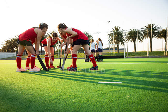 Side view of two teams of female Caucasian field hockey players, preparing before a game, huddling, motivating each other, on a sunny day — Stock Photo