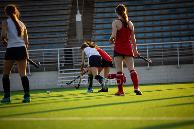Rear view of a Caucasian female field hockey player, during a field hockey game, running with a ball, holding a hockey stick, with her teammates and opponents in the foreground, on a sunny day — Stock Photo