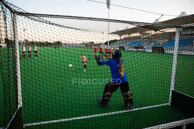 Rear view of a Caucasian female field hockey goalkeeper, during a field hockey game, standing in a goal, failing to defend a penalty kick, with her teammates and opponents in the background, on a sunny day — Stock Photo