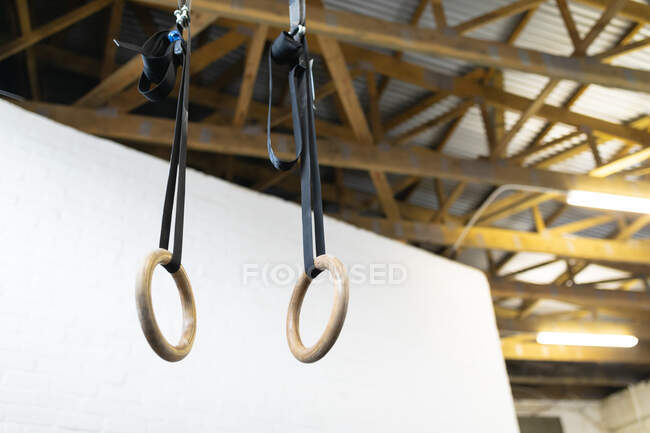 Vista de baixo ângulo de um par de anéis de ginástica de madeira pendurados em tiras ajustáveis de vigas de madeira no teto de um ginásio — Fotografia de Stock