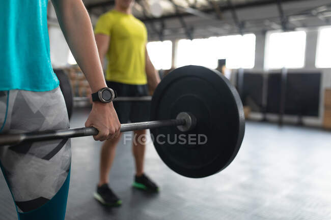 Front view mid section of an athletic Caucasian man and woman wearing sports clothes cross training at a gym, standing and weight training with barbells — Stock Photo