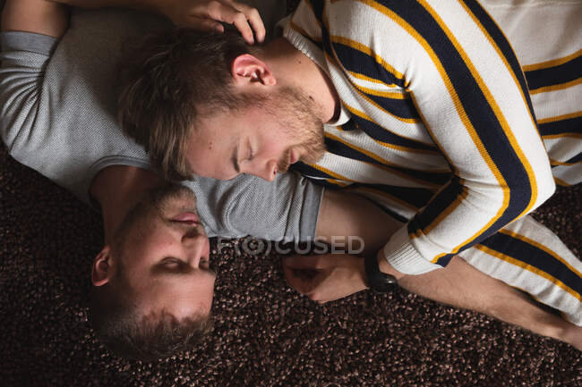 Großaufnahme von kaukasischen männlichen Pärchen, die es sich zu Hause gemütlich machen, auf einem Teppich liegen, sich umarmen und zusammen schlafen. — Stockfoto