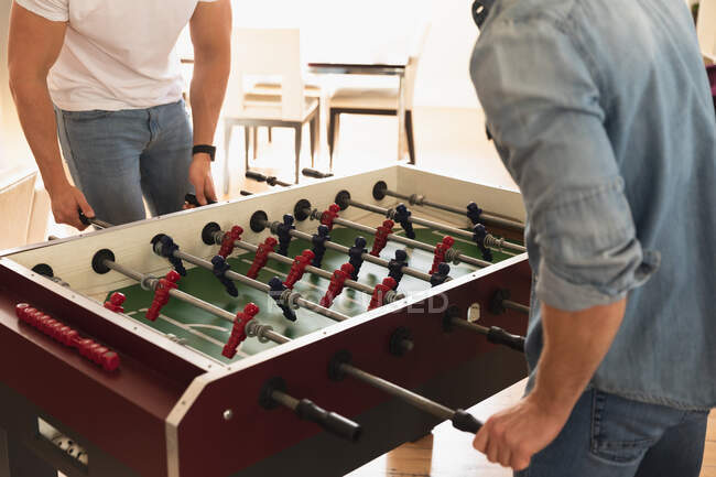 Side view mid section of male couple relaxing at home, standing in their living room, playing table football together. — Stock Photo