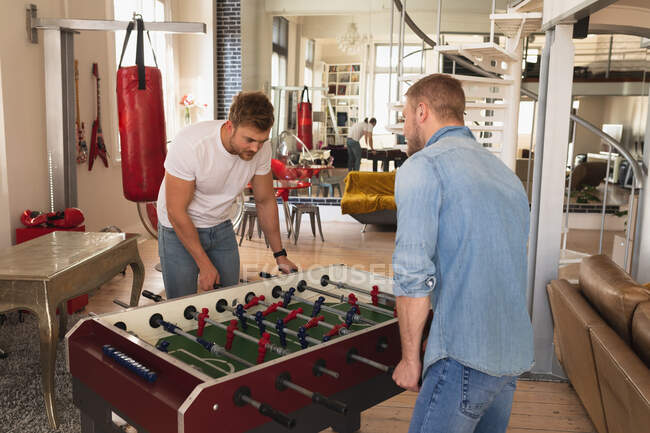 Side view of Caucasian male couple relaxing at home, standing in their living room, playing table football together. — Stock Photo